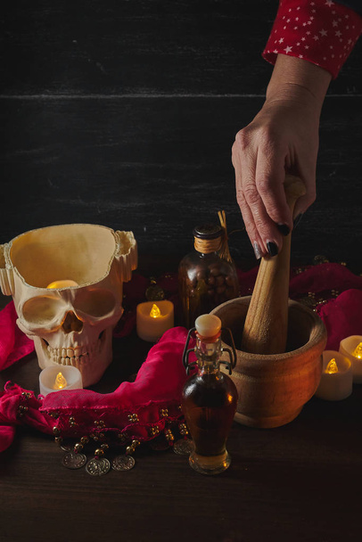 Hand using mortar Scary still life with potions, skull, mortar, vintage bottles and candles on witch table. Halloween or esoteric concept. - Photo, Image