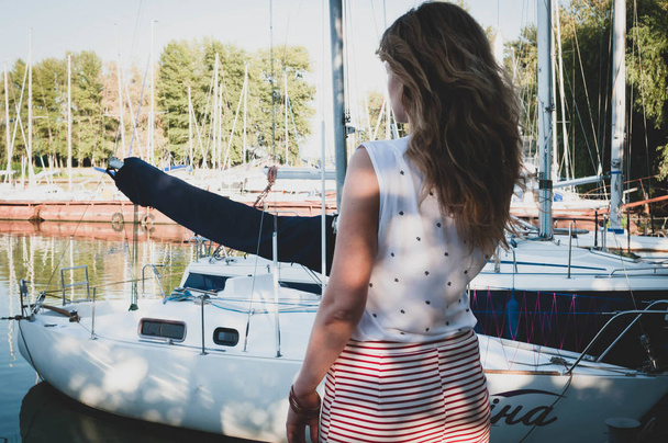 back view of woman with long hair in blouse and skirt standing and lookig away in front of sailboats in yachts club - Фото, зображення