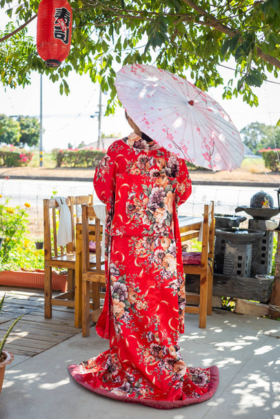 A lány egy piros hagyományos kimonót visel, ami Japán nemzeti ruhája, és egy esernyőt tart a kezében. - Fotó, kép