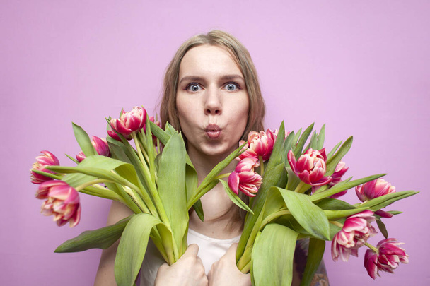 beautiful girl holding a bouquet of flowers on a pink background, happy woman with tulips surprised - Φωτογραφία, εικόνα