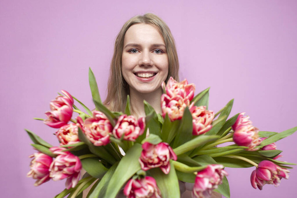girl holds and sniffs a bouquet of flowers on a pink background, a beautiful woman with tulips - Photo, Image