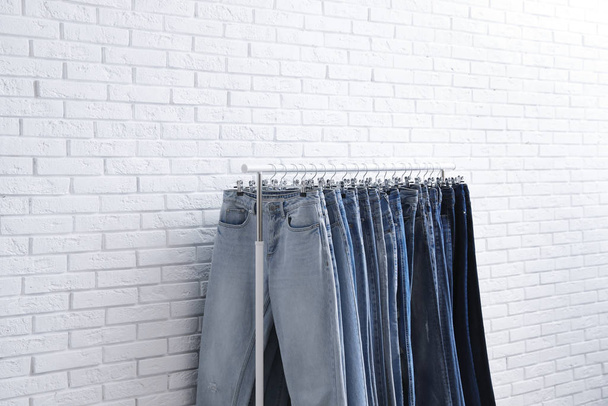 Rack with stylish jeans near brick wall - 写真・画像