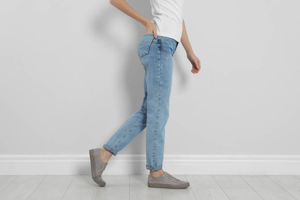 Young woman in stylish jeans near light wall, closeup - Foto, immagini