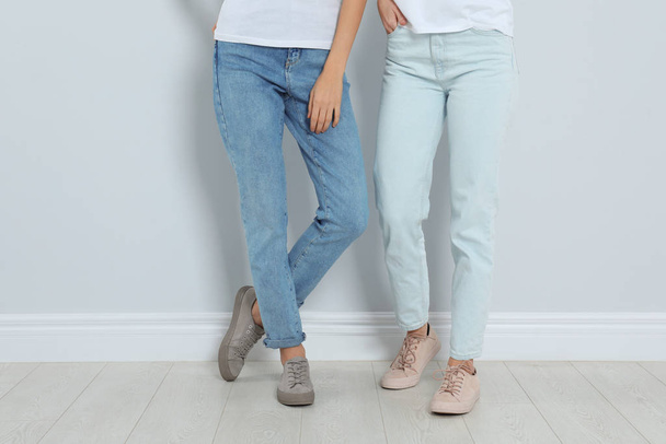Young women in stylish jeans near light wall, closeup - Foto, afbeelding