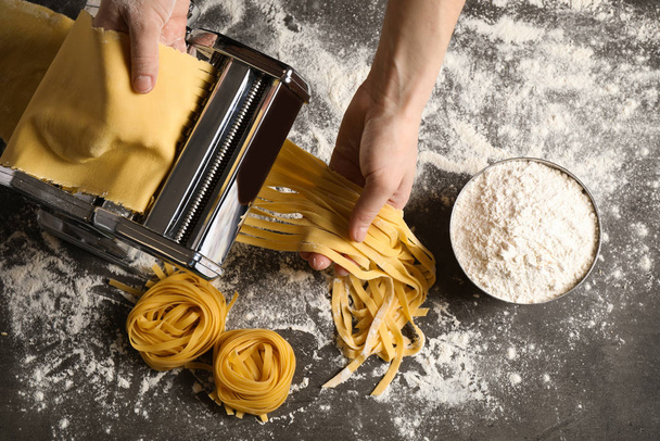 Woman preparing noodles with pasta maker machine at grey table,  - Foto, Bild