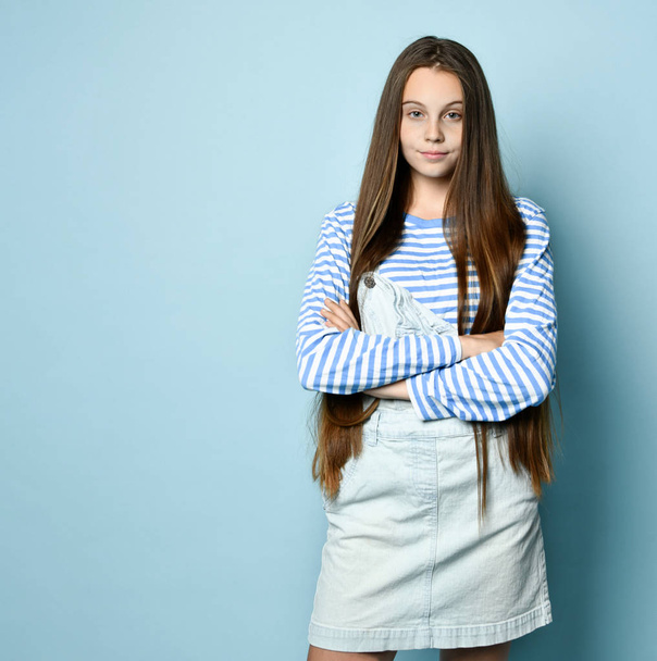 Teenage female in jeans overall and striped sweatshirt. She is smiling while posing against blue studio background. Close up - Fotó, kép