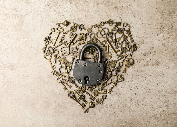 Heart made of keys and steel padlock on light stone background, top view. Safety concept - Foto, Imagem