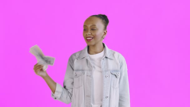 Satisfied african american woman with money is showing thumb up on pink background Jean jacket - Záběry, video