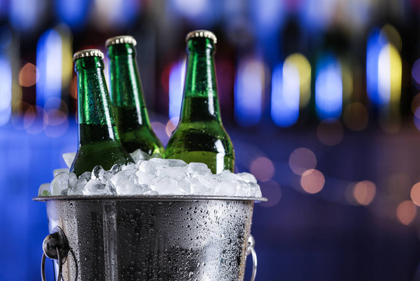 Beer in metal bucket with ice against blurred lights, closeup - Foto, Bild