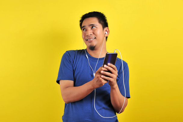 asiatischer Mann in lässigem blauem T-Shirt mit Headset, der Musik hört - Foto, Bild