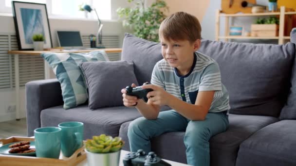 Joyful child enjoying video game in apartment having fun relaxing on sofa - Video, Çekim