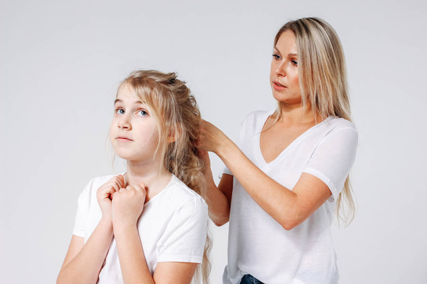 Young beautiful blonde woman make hair style for girl. Joint leisure of mother and daughter. Isolated on white background - Photo, Image
