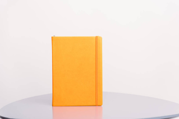 Πορτοκαλί βιβλίο, ατζέντα ή σχεδιαστής στέκεται σε μια γκρι επιφάνεια και λευκό φόντο. Πρότυπο βιβλίου. - Φωτογραφία, εικόνα