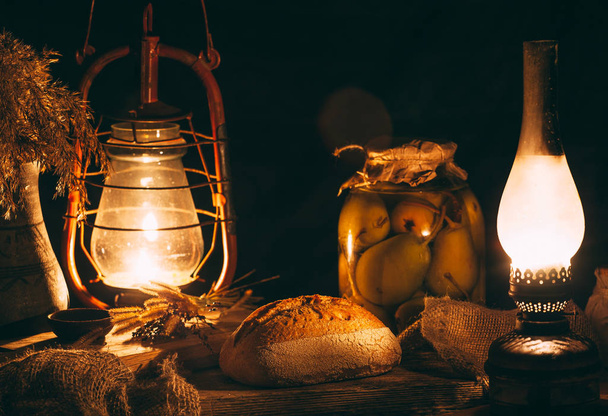 Homemade baked bread on a wooden board in warm light from gas lamps. Rustic vintage surroundings - Photo, Image