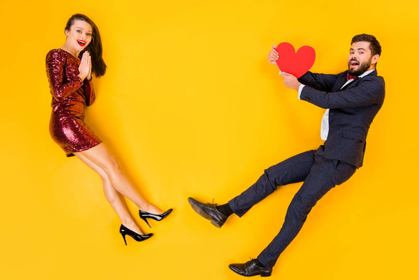 Top above high angle view full body profile side photo of two people romance date man catch red big paper card heart woman amazed wear suit bowtie lay isolated yellow color background - Foto, imagen