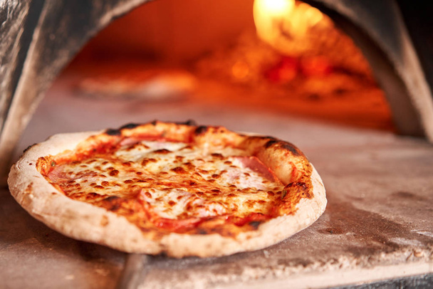 Baked tasty margherita pizza in Traditional wood oven in Naples restaurant, Italy. Original neapolitan pizza. Red hot coal. - Photo, Image