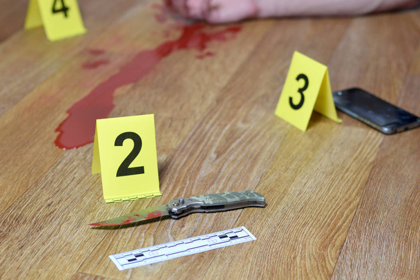 Crime scene investigation - Bloody knife and victims hand with yellow criminal markers on kitchen floor - Photo, Image