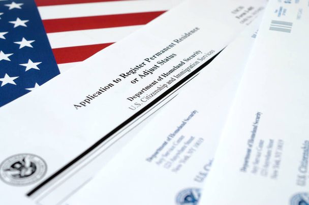 I-485 Заявление на регистрацию постоянного места жительства или изменение статуса бланка лежит на флаге США с конвертом от Министерства внутренней безопасности
 - Фото, изображение
