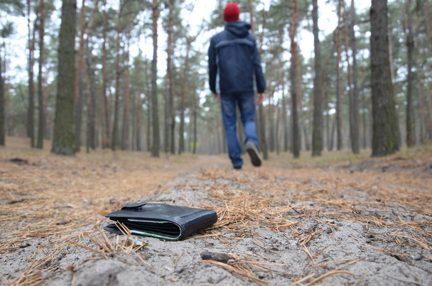 若い男はロシアの秋のモミの木の道にユーロ紙幣で財布を失う。不注意で財布の概念を失う - 写真・画像
