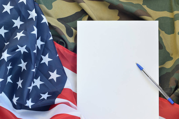 Blank paper lies on United States of America flag and folded military uniform jacket. Military symbols conceptual background banner and copy space - Photo, Image