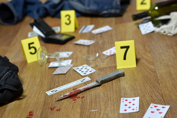 Vyšetřování místa činu - očíslování důkazů po vraždě v bytě. Spousta hracích karet s oblečením, peněženkou a lahví vína jako důkaz - Fotografie, Obrázek