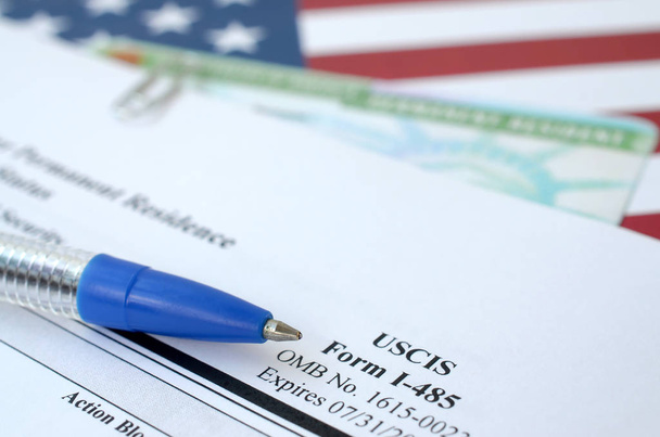 I-485 Aanvraag om permanent verblijf te registreren of aan te passen statusformulier en groene kaart van dv-loterij ligt op de vlag van de Verenigde Staten met blauwe pen van het ministerie van Binnenlandse Veiligheid - Foto, afbeelding