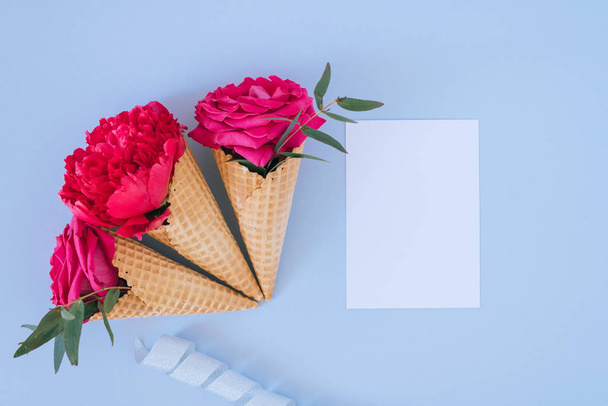 Platte lay Ice Cream kegels met roze pioen en rozen en wit duidelijk leeg voor tekst op blauwe achtergrond. - Foto, afbeelding