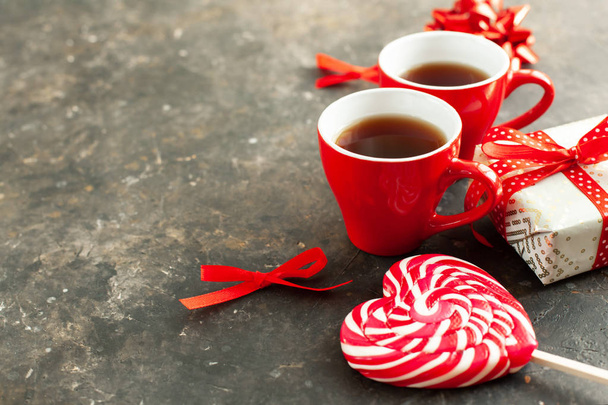 Две красные чашки горячего эспрессо или кофе, красивый завернутый подарок, бело-красный леденец в форме сердца и декоративные бантики, enpty пространство для текста. День святого Валентина романтическое свидание концепции, крупным планом
 - Фото, изображение