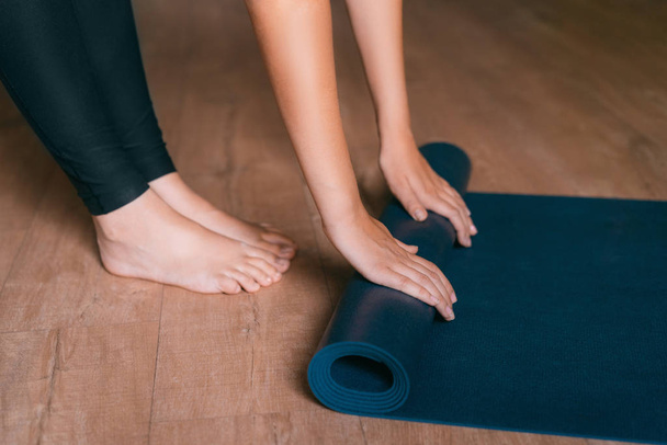 Woman folding blue exercise mat on wooden floor. - Photo, image