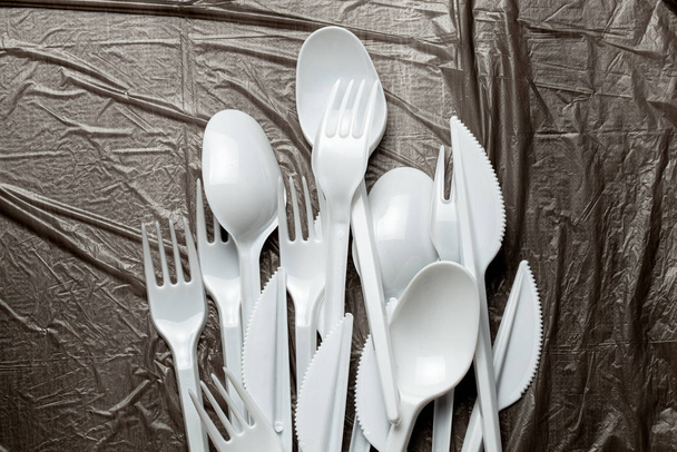 Plastic cutlery, forks, spoons and knives. Pollution of the environment with plastic and microplastics. Black plastic background - Photo, Image