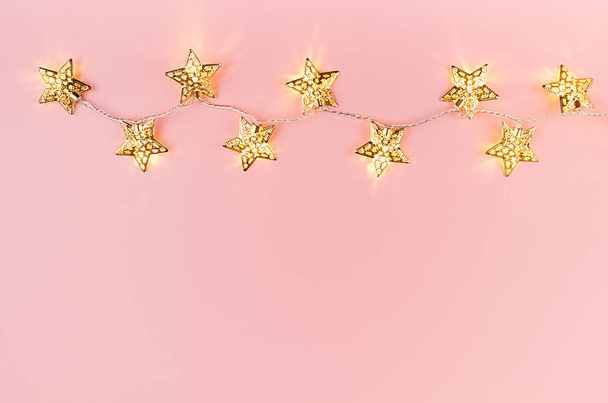 Christmas lights with golden stars glowing on soft light pastel pink background, border, copy space, top view. - Fotó, kép