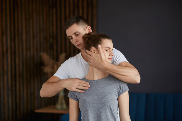 Female patient doing physical exercises with physiotherapist. Male therapist treating injured neck of young athlete. Post traumatic rehabilitation, sport physical therapy, recovery concept - Photo, image