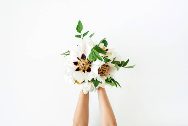 Manos de mujer sosteniendo flores de peonías blancas sobre fondo blanco. Asiento plano, vista superior. Composición floral mínima
. - Foto, Imagen