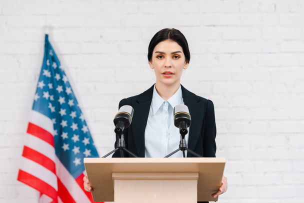 beautiful speaker talking near microphones and american flag  - Photo, Image