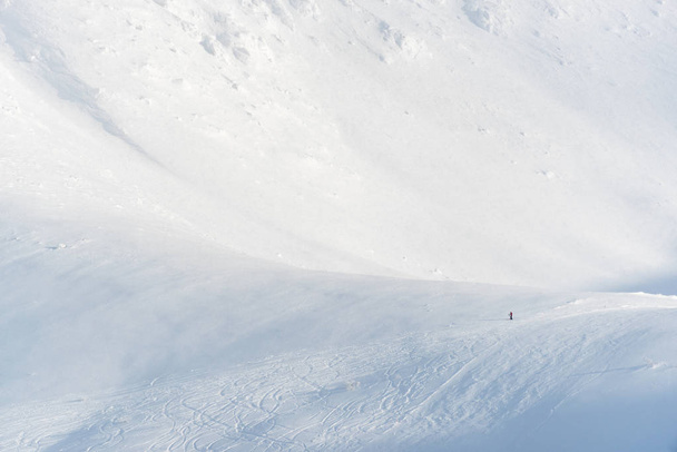 Bir kayak merkezinde dağlarda dinlenen yalnız bir kayakçı. Küçük kayakçı ölçek duygusu veriyor.. - Fotoğraf, Görsel
