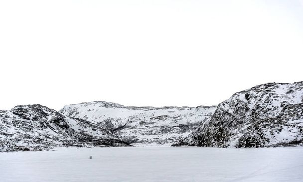 Caminhando sobre branco. Duas pessoas Nordic andando em um lago congelado ou campo cercado por colinas cobertas de neve sob um céu branco
 - Foto, Imagem