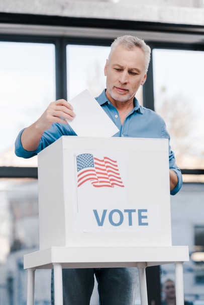  bebaarde man stemt en zet stembiljet in doos met stembelettering  - Foto, afbeelding