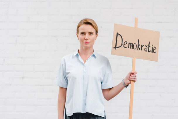 attractive woman holding placard with demokratie lettering near brick wall  - Φωτογραφία, εικόνα