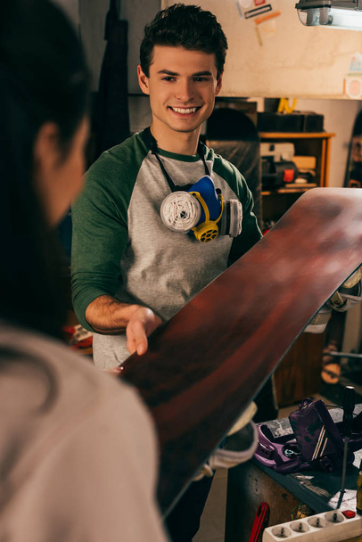 Ausgeschnittene Ansicht einer Frau, die lächelnden Arbeitern in der Werkstatt ein Snowboard reicht  - Foto, Bild