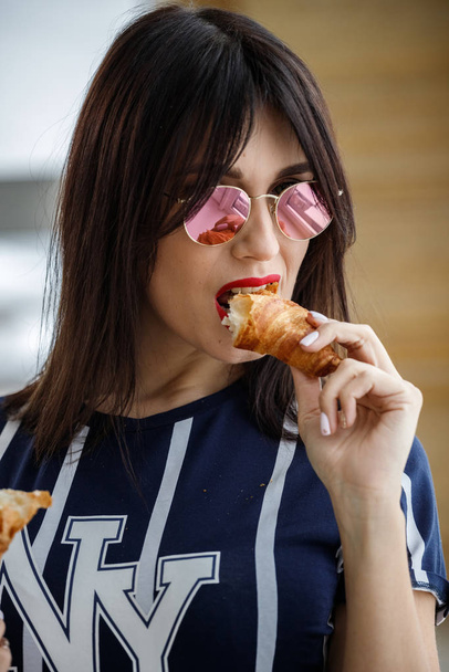Beautiful brunette girl in glasses eating croissant at apartment interior  - Foto, Bild