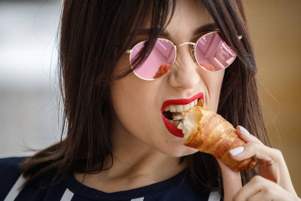 Beautiful brunette girl in glasses eating croissant at apartment interior  - Foto, immagini