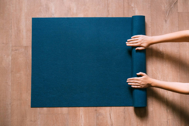Woman folding blue exercise mat on wooden floor. - Zdjęcie, obraz