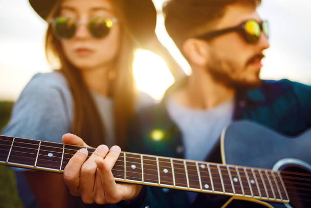 Man playing guitar to his girl on a picnic in park sitting on grass.  Young ouple enjoying party in the summer park. Rest, fun, summer  time together concept. - Foto, imagen