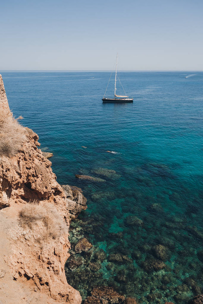 hügelige Küste von Mallorca. Im Hintergrund eine kleine Jacht auf dem Meer. im Vordergrund Klippe und kristallklares Wasser. Sommerliche Szenerie, - Foto, Bild