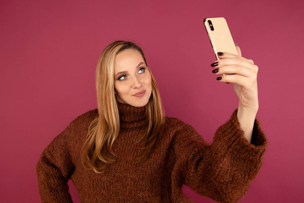 Giovane signora in maglione facendo foto di sé al telefono in studio rosa
. - Foto, immagini