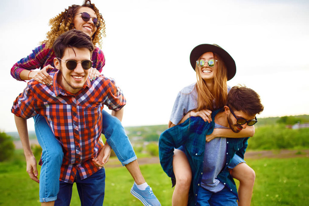 A guy carrying a girl on his back, smiling and relax. Teenagers having fun together in summer park. Group of young people enjoying party. Rest, fun, summer, holidays concept. - Foto, imagen