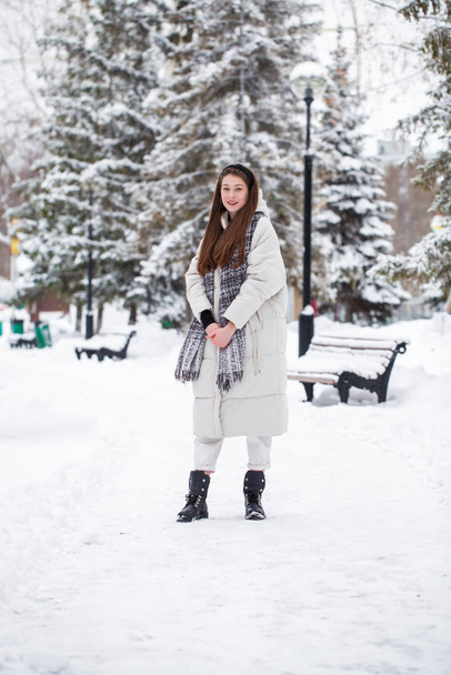 Young brunette woman in white down jacket in winter street - Фото, изображение