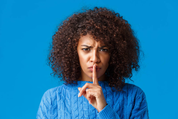 Close-up portrait offended and upset silly timid african-american girl frowning displeased, shushing angry at camera with index finger pressed lip, demand silence, asking keep quiet, blue background - Fotoğraf, Görsel