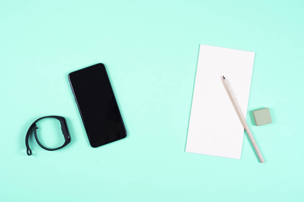 A modern smartphone lies on a paper Notepad, next to a pencil and eraser. minty background. - Zdjęcie, obraz