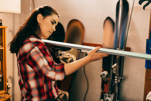 attractive woman holding and looking at ski in repair shop  - 写真・画像